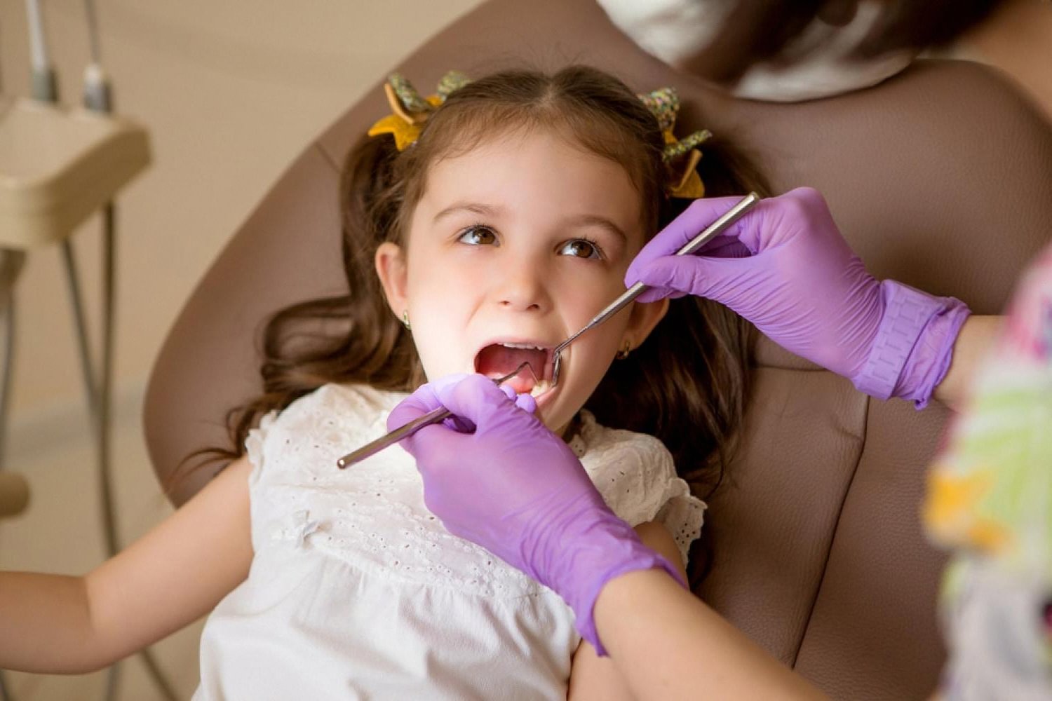 Young girl having her teeth checked by a dentist wearing purple gloves during a kids dental visit