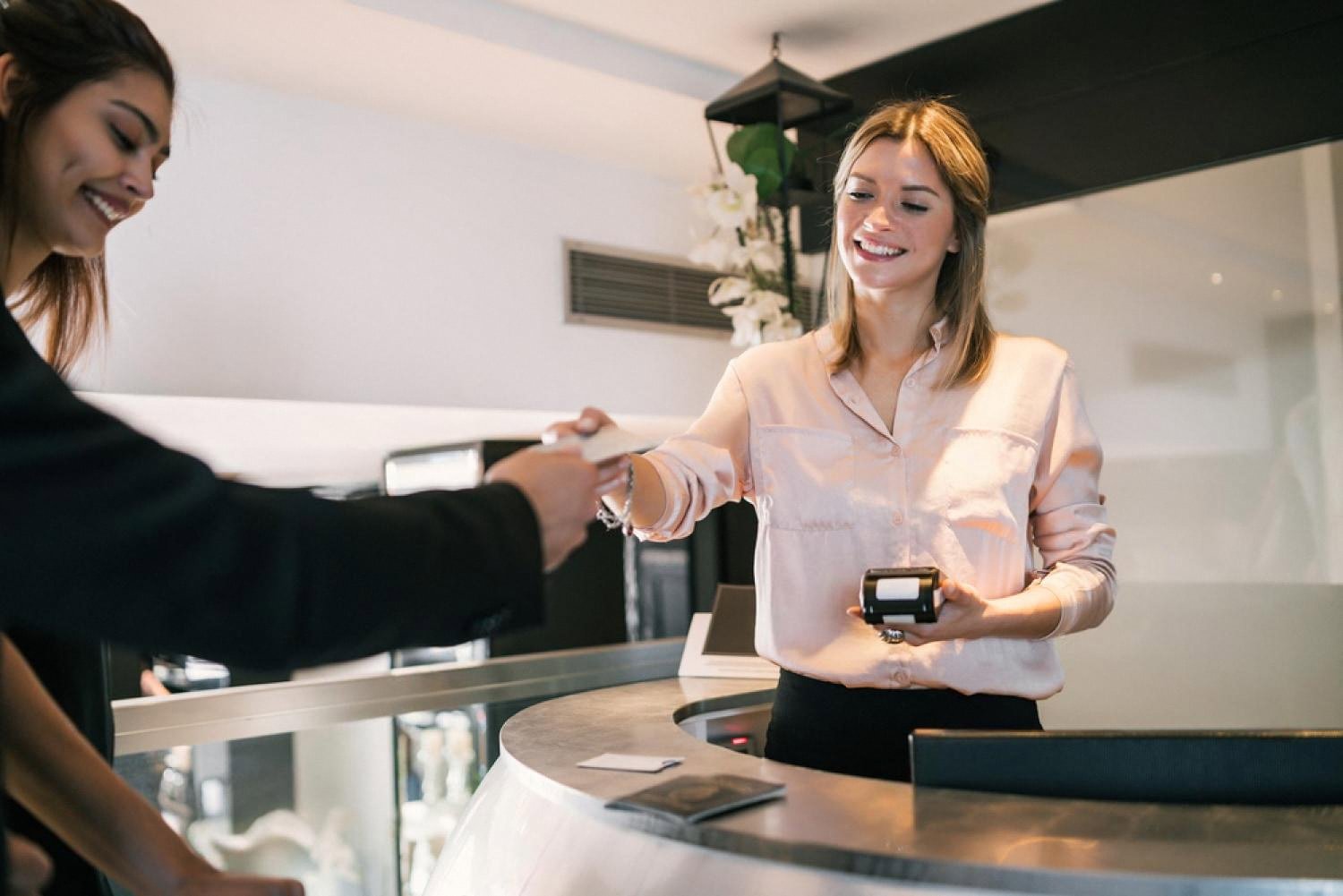 Smiling receptionist handing back a key card to a guest at a Dubai hotel front desk